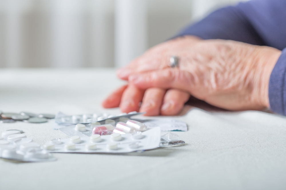 Elderly hand resting near pill blister packs on light table.